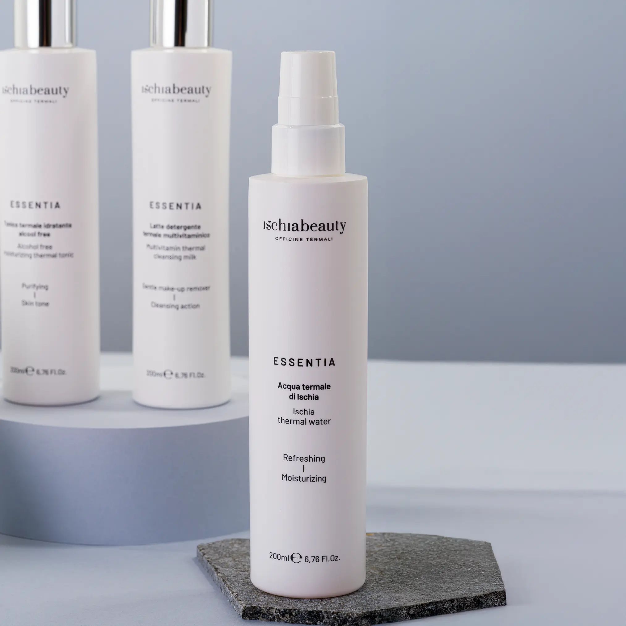 Drei weiße Sprays mit 'ischiabeauty' und 'ESSENTIA'. 'Acqua termale di Ischia'. Auf Steinplatte platziert.