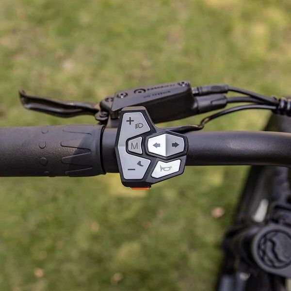 Fahrradlenker mit Bedienelementen. Tasten für Funktionen, Pfeiltasten, Hupe. Schwarzes Gehäuse.