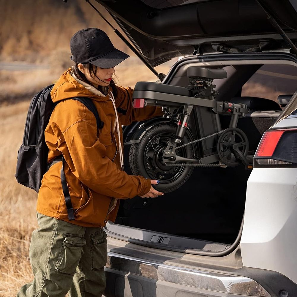 Frau entnimmt ein zusammengeklapptes E-Bike aus einem Kofferraum. Schwarzes Fahrrad.