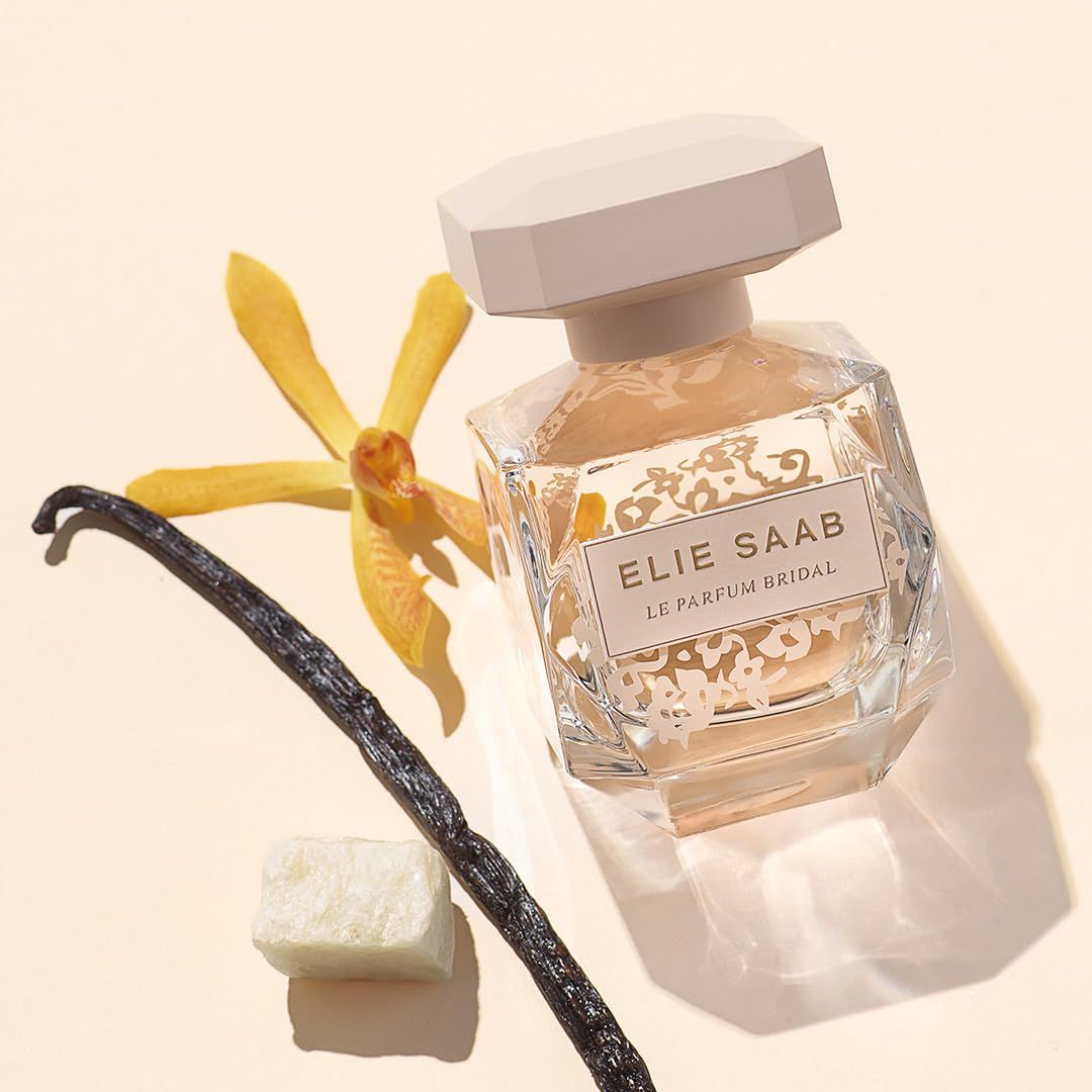 Glasflakon mit beigem Deckel, ELIE SAAB Le Parfum Bridal. Vanilleschote, Blüte und Würfel daneben.