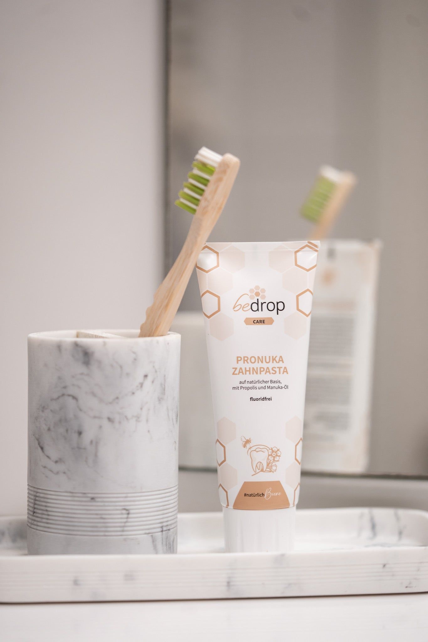 Tube bedrop Pronuka Zahnpasta neben Zahnbürste und Marmor-Becher. Tube weiß mit braunen Akzenten und Produktinformationen. Aufschrift: Pronuka Zahnpasta.