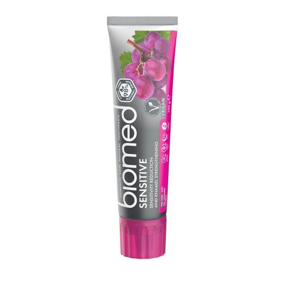 Zahnpasta-Tube mit "biomed Sensitive"-Aufdruck, lila Kappe und Trauben-Illustration. Vegan-Siegel und Qualitätszeichen.