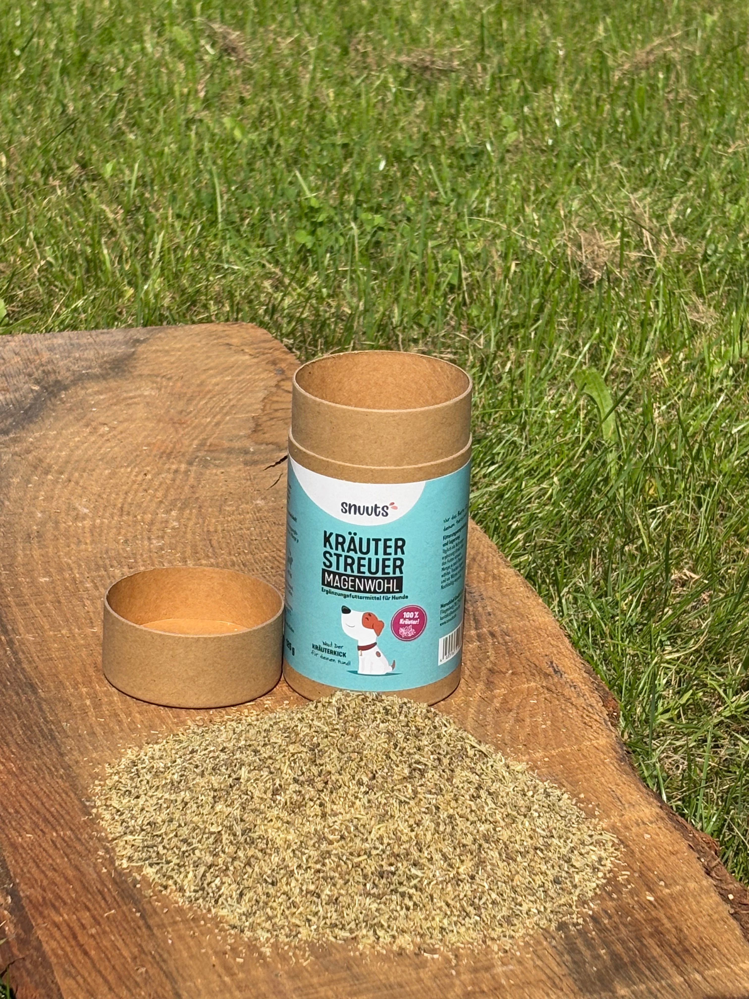 Zylindrische Pappdose, Schale und Kräuterhaufen auf Holz. Aufschrift 'snuuts Kräuterstreuer Magenwohl'.