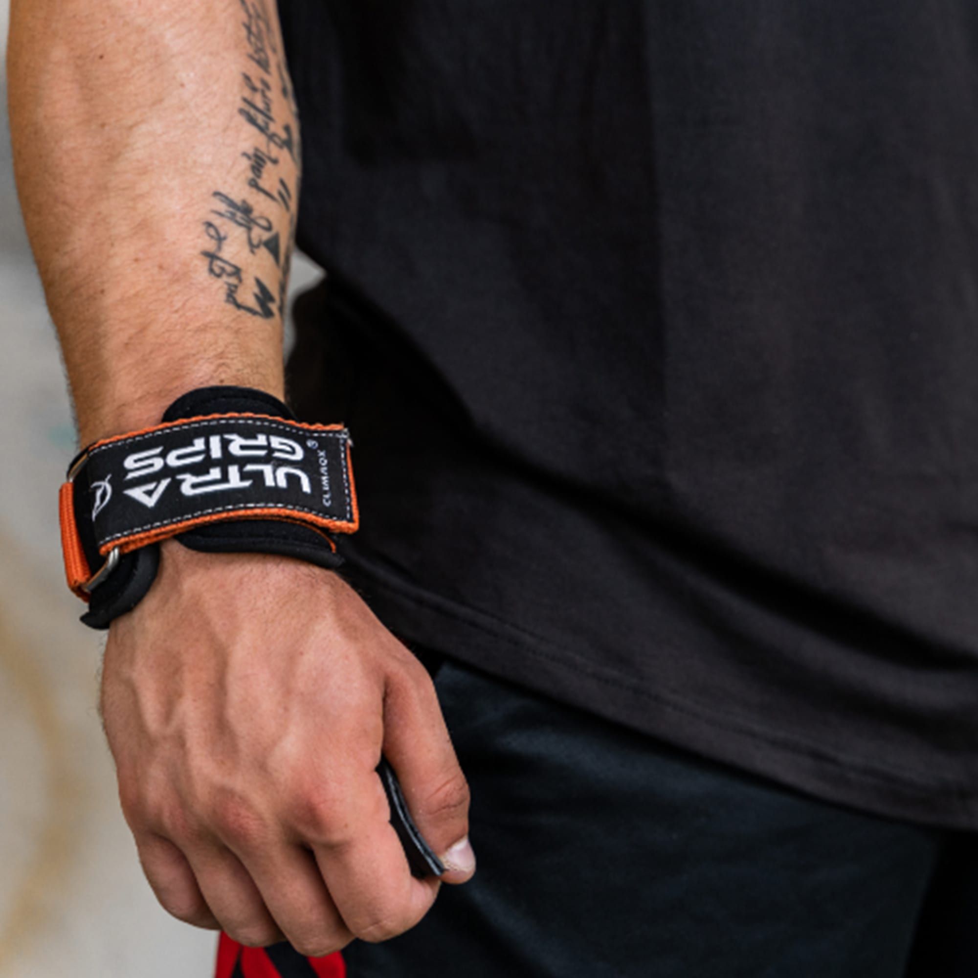 Nahaufnahme eines Handgelenks mit Ultra-Grips. Schwarzes Band mit "ULTRA GRIPS" und orangefarbenen Details.