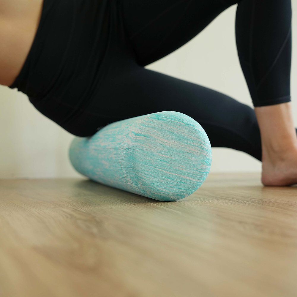 Zylindrischer Pilates-Roller, blau-weiß marmoriert, auf Holzfußboden. Person stützt sich mit Bein auf dem Roller ab.