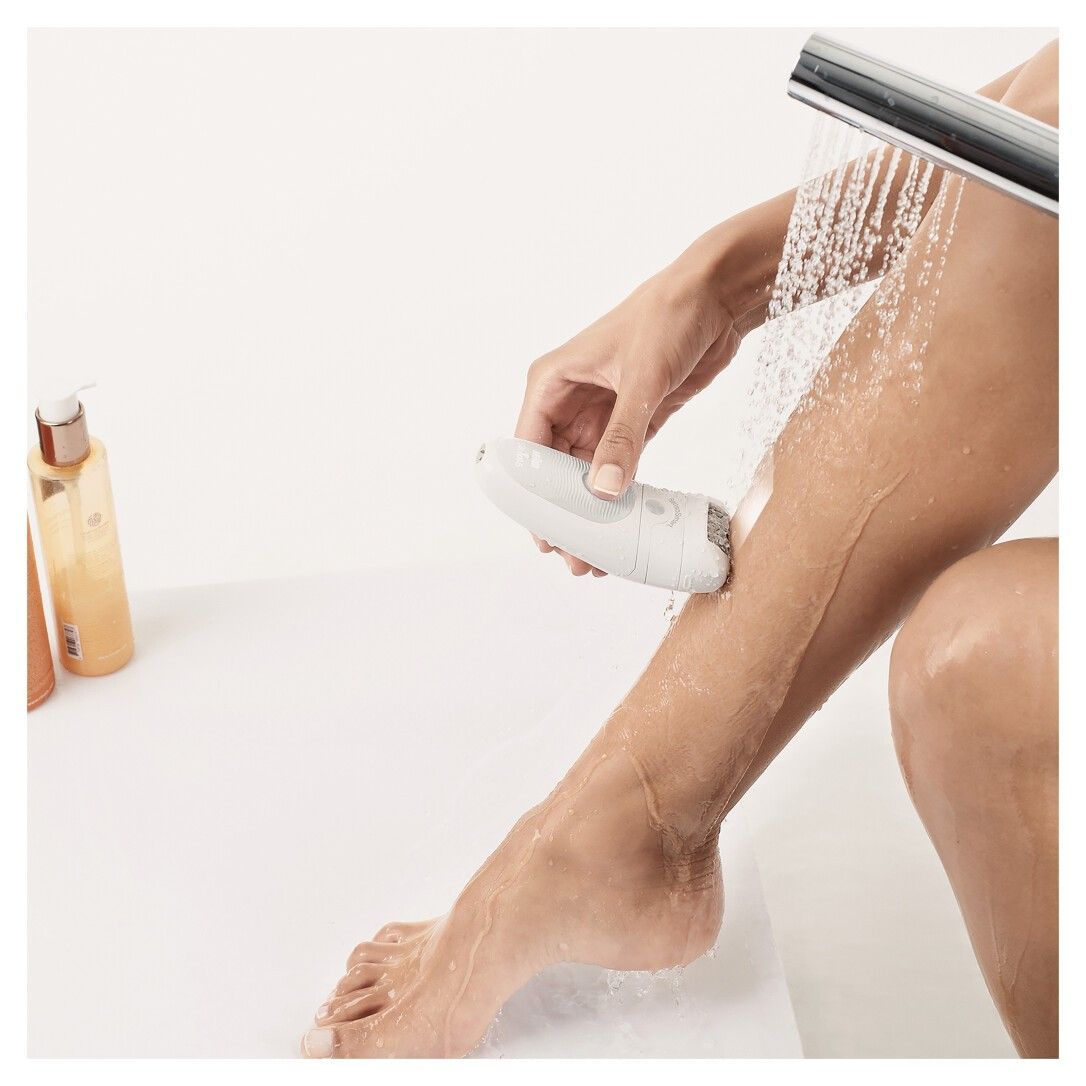 Eine Person epiliert ein Bein unter der Dusche. Der Epilierer ist weiß.