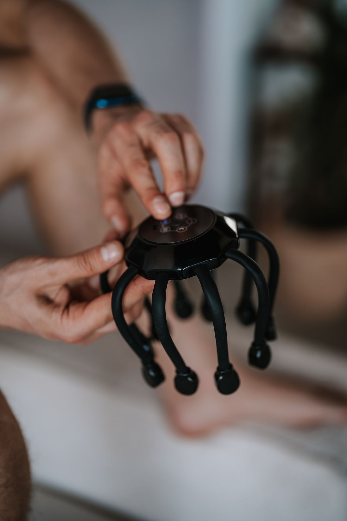 Person hält ein schwarzes Kopfmassagegerät. Gerät mit acht flexiblen Armen.