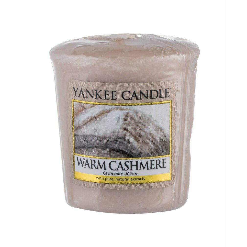 Verpackte beige Duftkerze mit Etikett. Aufschrift: Yankee Candle, Warm Cashmere. Abbildung von Decken. Mit Docht.
