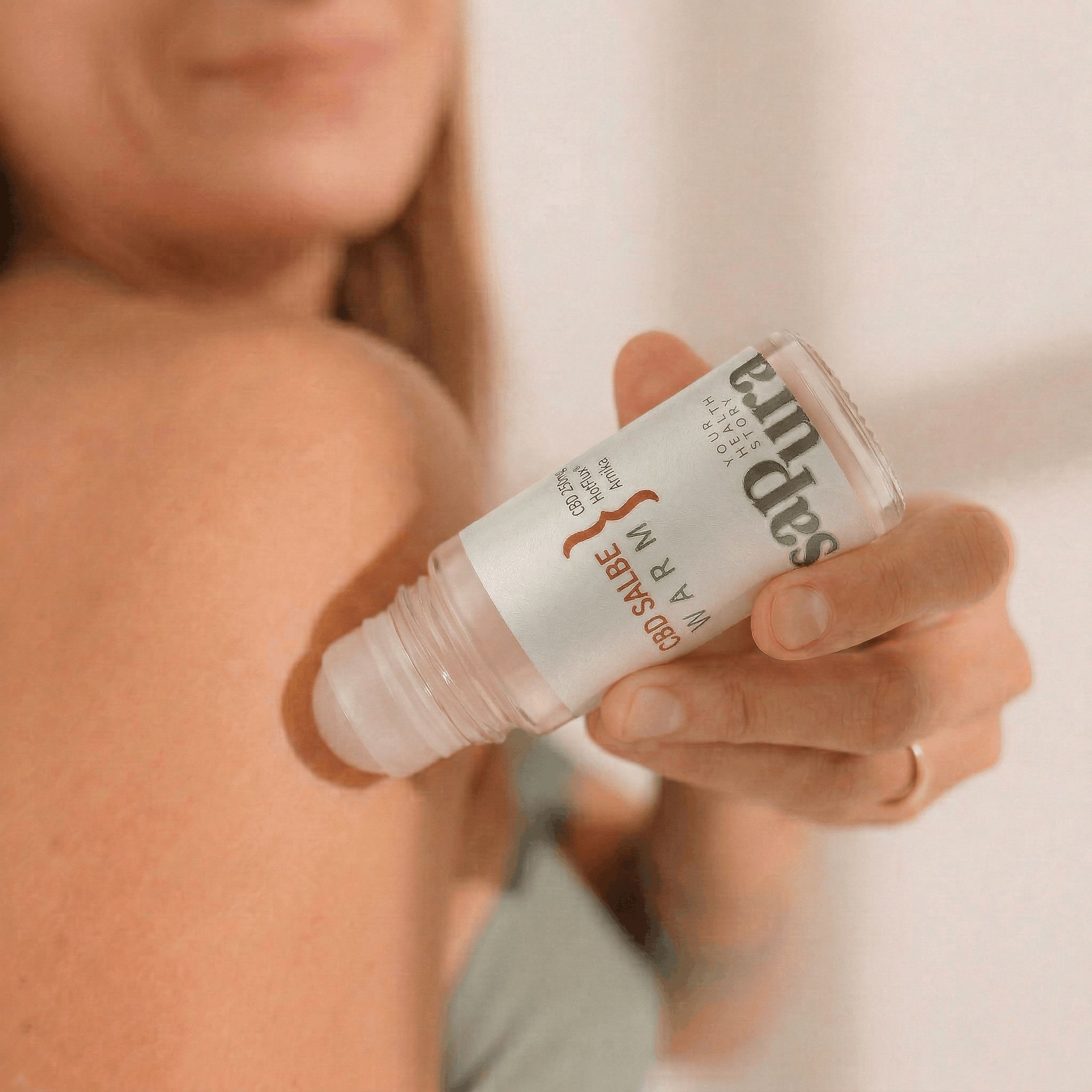 Hand hält SAPURA® CBD Wärmesalbe Roll-On Flasche am Rücken.