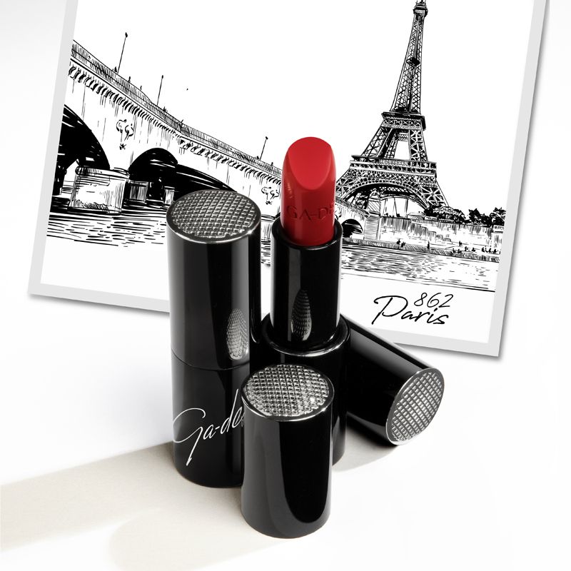 Roter Lippenstift, geöffnet. Schwarze Hülsen mit silbernen Deckeln. Ga-De-Logo. Hintergrund: Paris-Illustration.