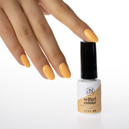 Hand mit orange lackierten Nägeln neben einer Nagellackflasche. Flasche mit schwarzer Kappe, weißem Etikett mit Logo und Produktnamen.