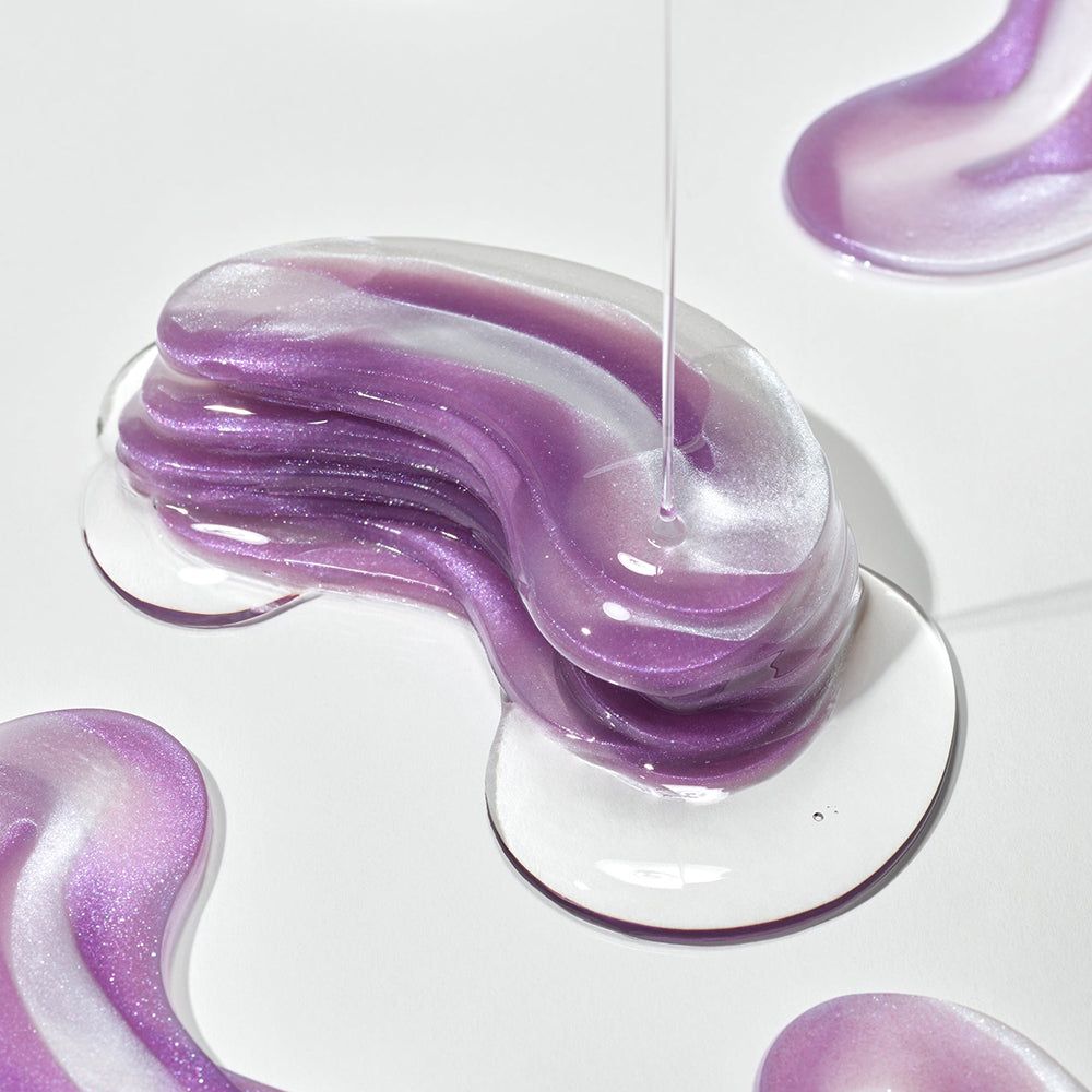 Lila-weiße Hydrogel-Augenpads mit Glitzer, aus denen klare Flüssigkeit tropft, auf weißem Hintergrund.