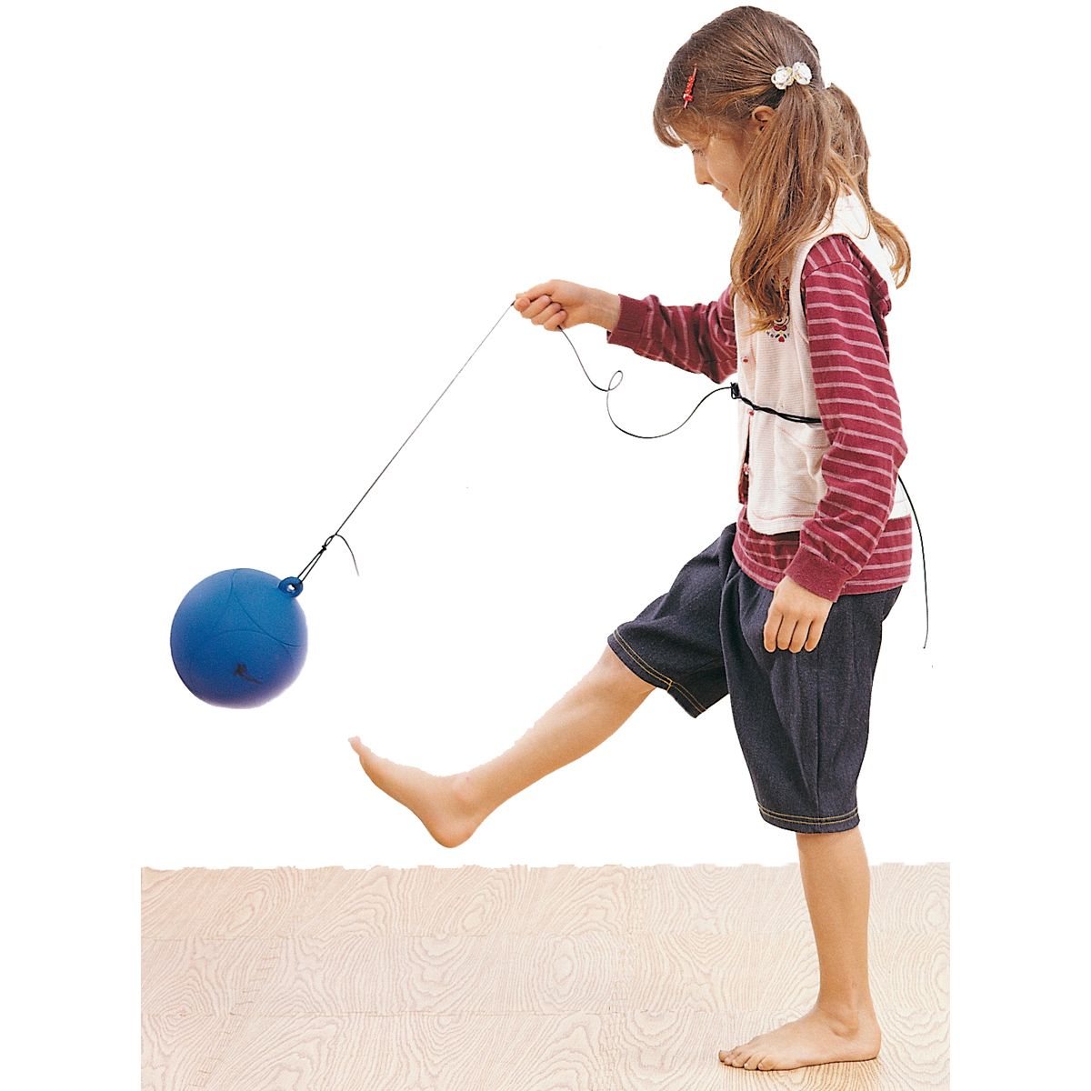 Kind tritt blauen Ball. Ball an Schnur. Kind trägt Shorts.