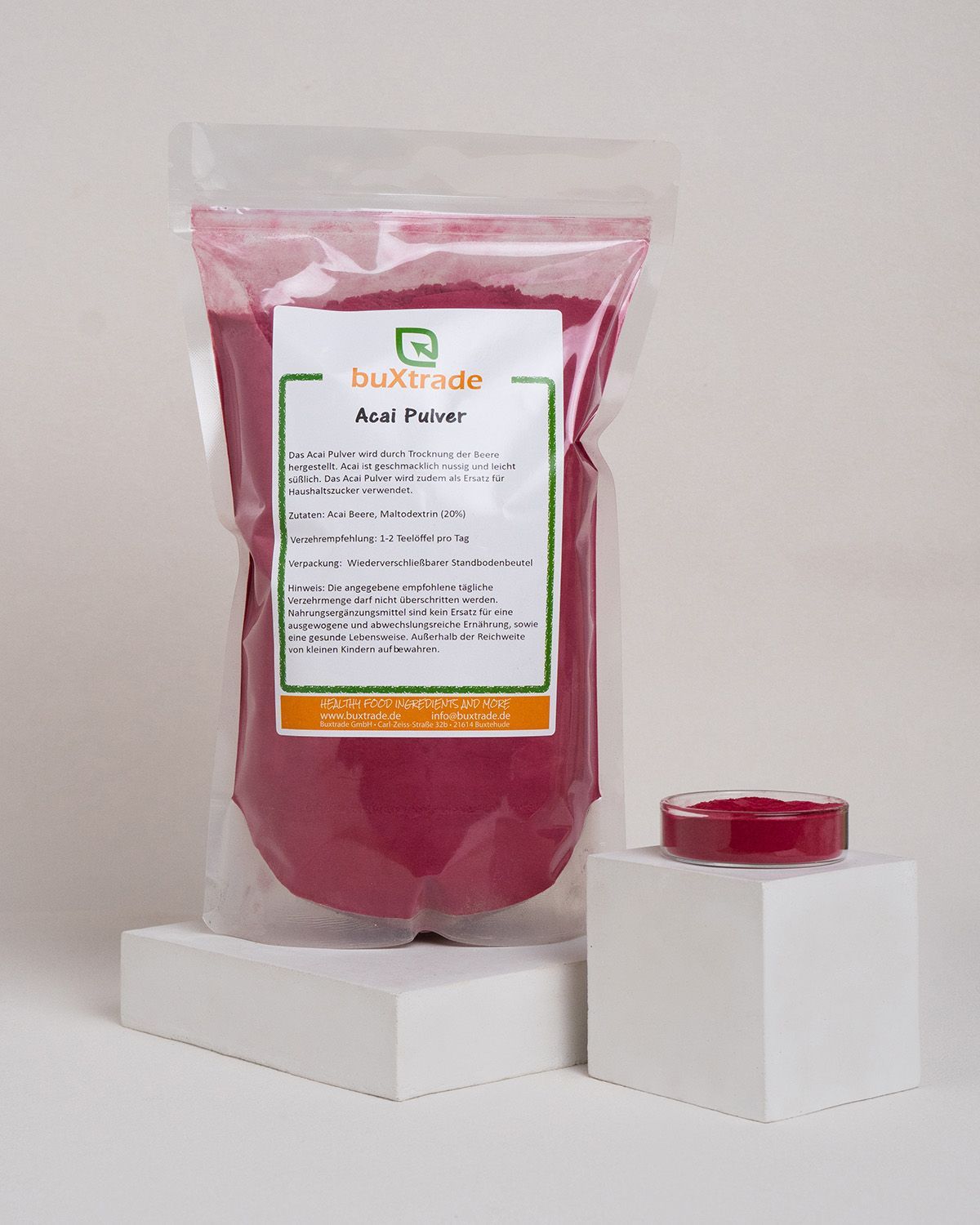 Transparenter Beutel mit rotem Pulver und Etikett, daneben eine kleine Schale mit Pulver. Auf dem Etikett steht 'buXtrade Acai Pulver'.