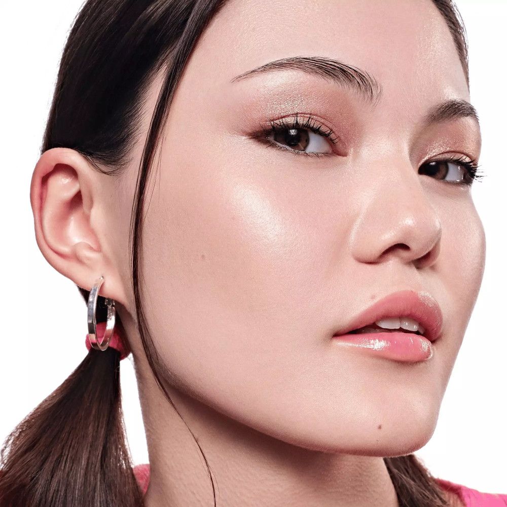 Porträt einer Frau mit hellem Teint. Goldfarbener Lidschatten, rosa Lippen. Haare zurückgebunden, Ohrringe.