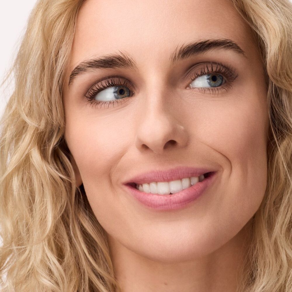 Porträt einer Frau mit blonden Locken, die zur Seite schaut. Sie trägt Make-up.