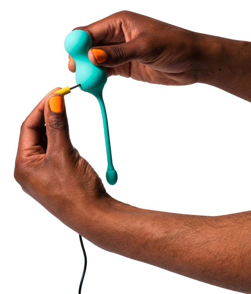 Hände halten ein türkisfarbenes Produkt. Ein Kabel wird in das Produkt gesteckt. Gelb lackierte Nägel.