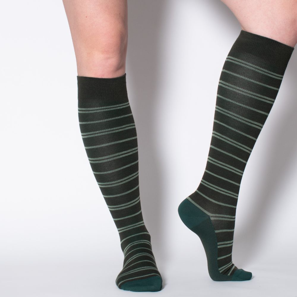 Zwei grüne Kniestrümpfe mit helleren Streifen. Dunkelgrüne Ferse und Zehenbereich. Nahaufnahme, Beine vor weißem Hintergrund.