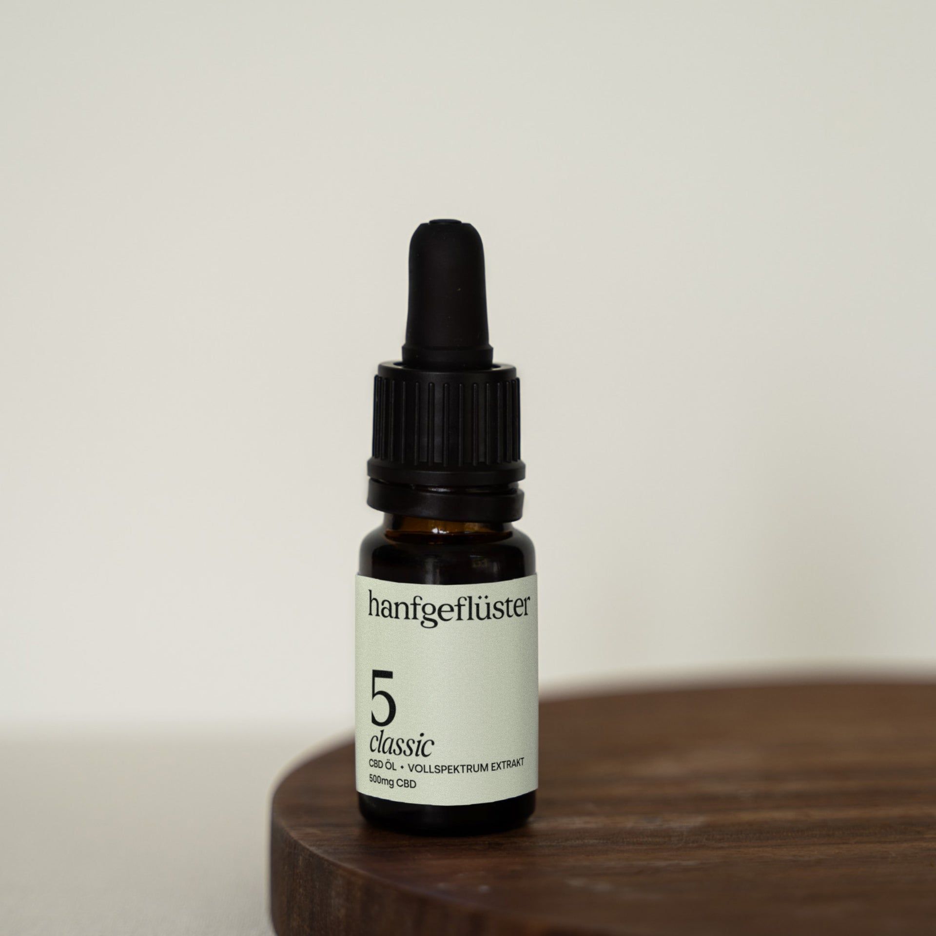 Braune Glasflasche mit schwarzem Tropfer. Etikett mit "hanfgeflüster", "5 classic" und "CBD-ÖL". Auf Holzuntergrund.