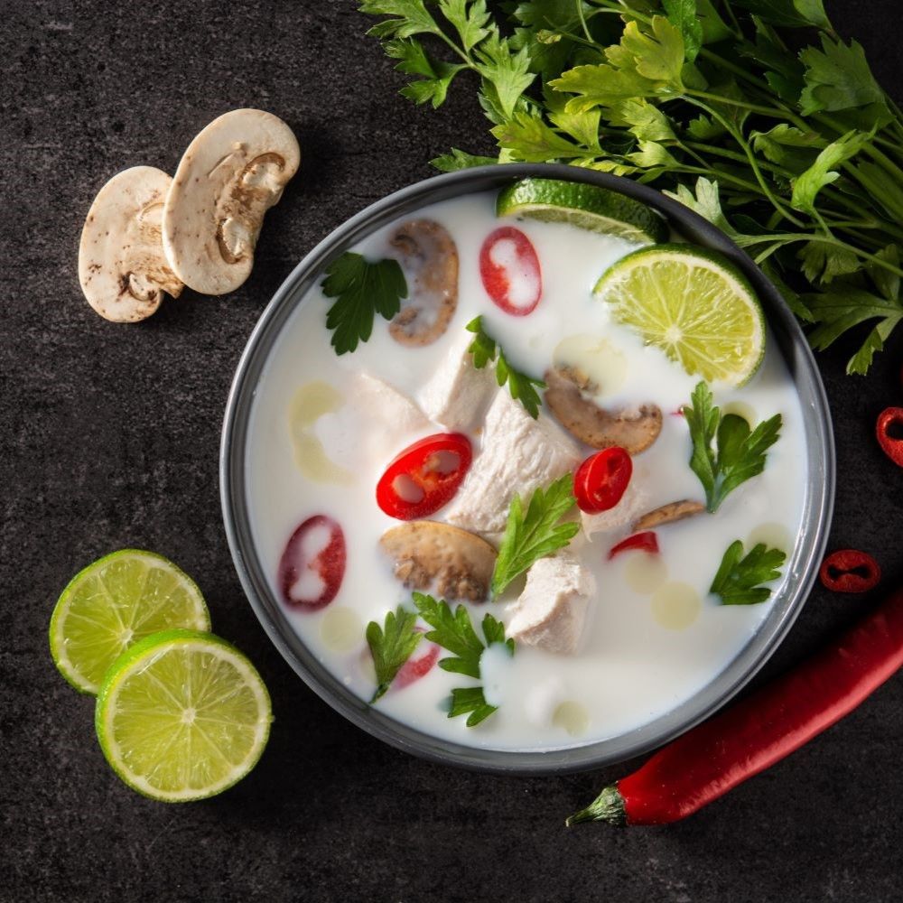 Suppe mit Hühnchen, Pilzen, Limetten, Chili und Kräutern. Auf dunklem Untergrund. Draufsicht.