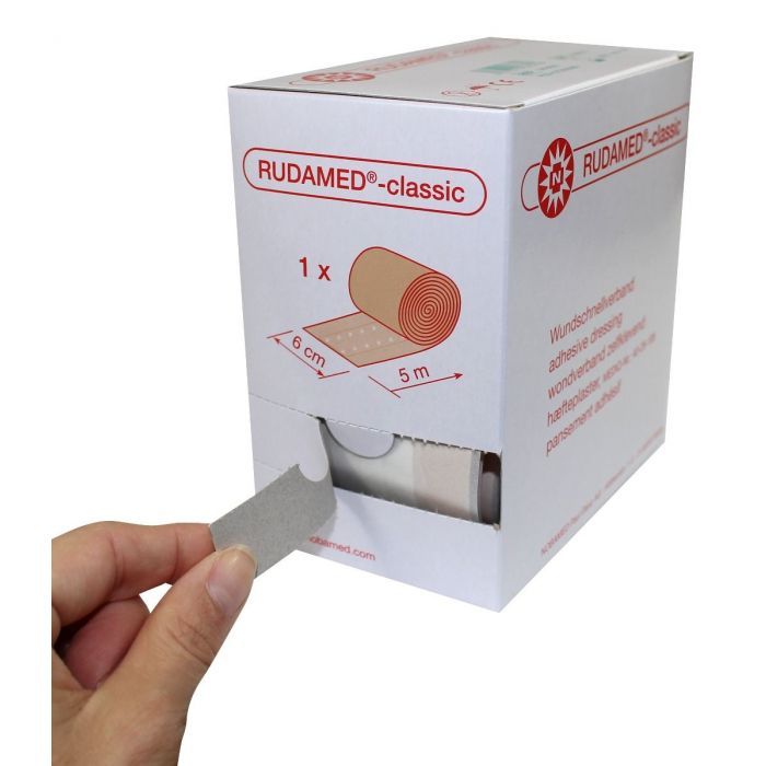 Rudamed-classic Wundpflaster-Verpackung. Hand entnimmt Pflaster. Aufschrift: Wundschnellverband, 6 cm x 5 m.