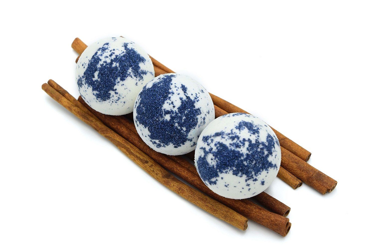 Drei runde, weiße Badebomben mit blauer Verzierung, auf Zimtstangen platziert. Nahaufnahme, isoliert auf weißem Hintergrund.
