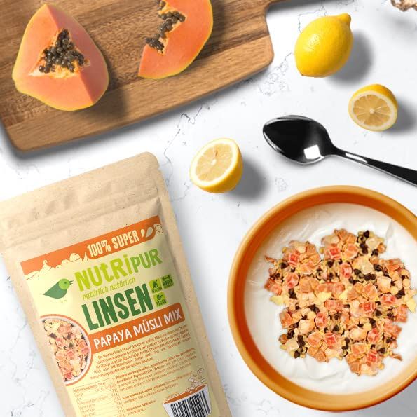 Packung NutriPur Linsen Papaya Müsli Mix neben Schüssel mit Müsli, Papaya-Stücke, Zitronen und Löffel.