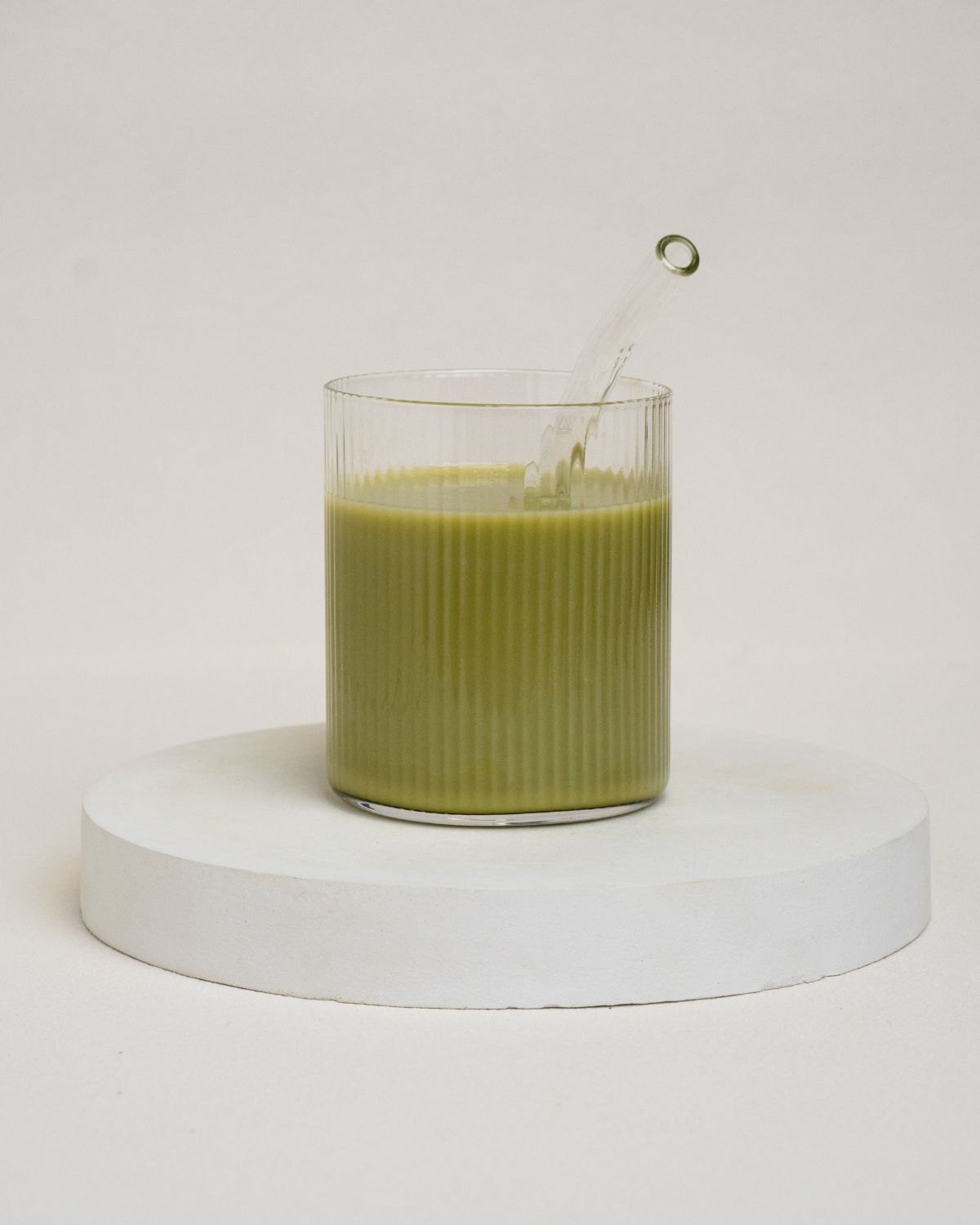 Geriffeltes Glas mit grünem Getränk und Glasstrohhalm.