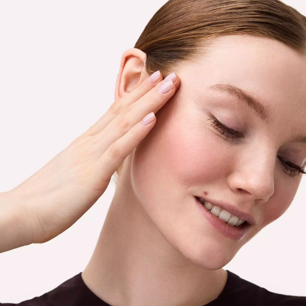 Frau berührt sanft ihre Wange. Rouge auf den Wangen. Geschlossene Augen.