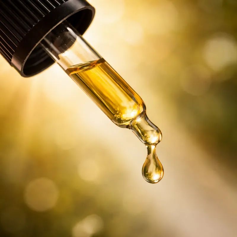 Pipette mit goldenem flüssigem Tropfen, Sonnenlicht im Hintergrund.