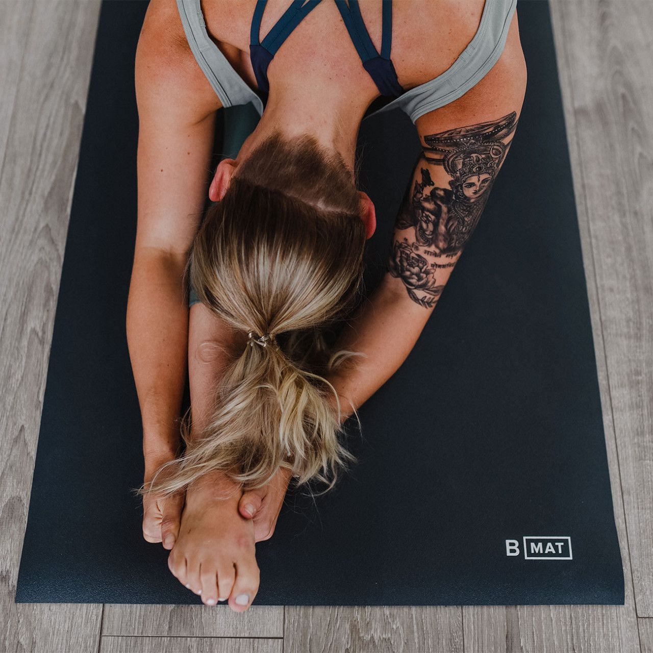 Person in Yoga-Position auf anthrazitfarbener Matte. Das Logo "b.mat" ist sichtbar.