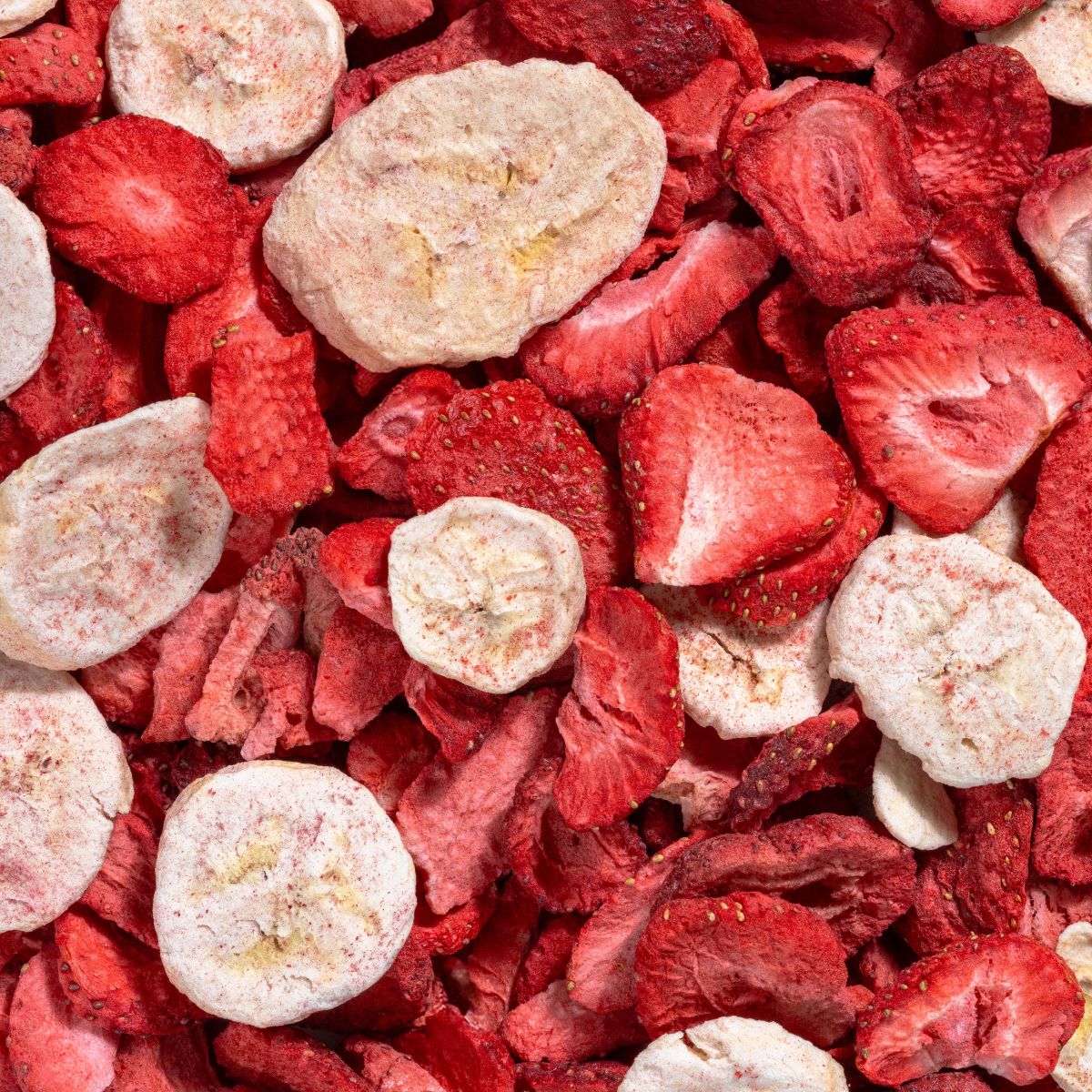 Nahaufnahme von gefriergetrockneten Erdbeeren und Bananenscheiben. Rote und beige Farben. Unterschiedliche Formen und Größen.
