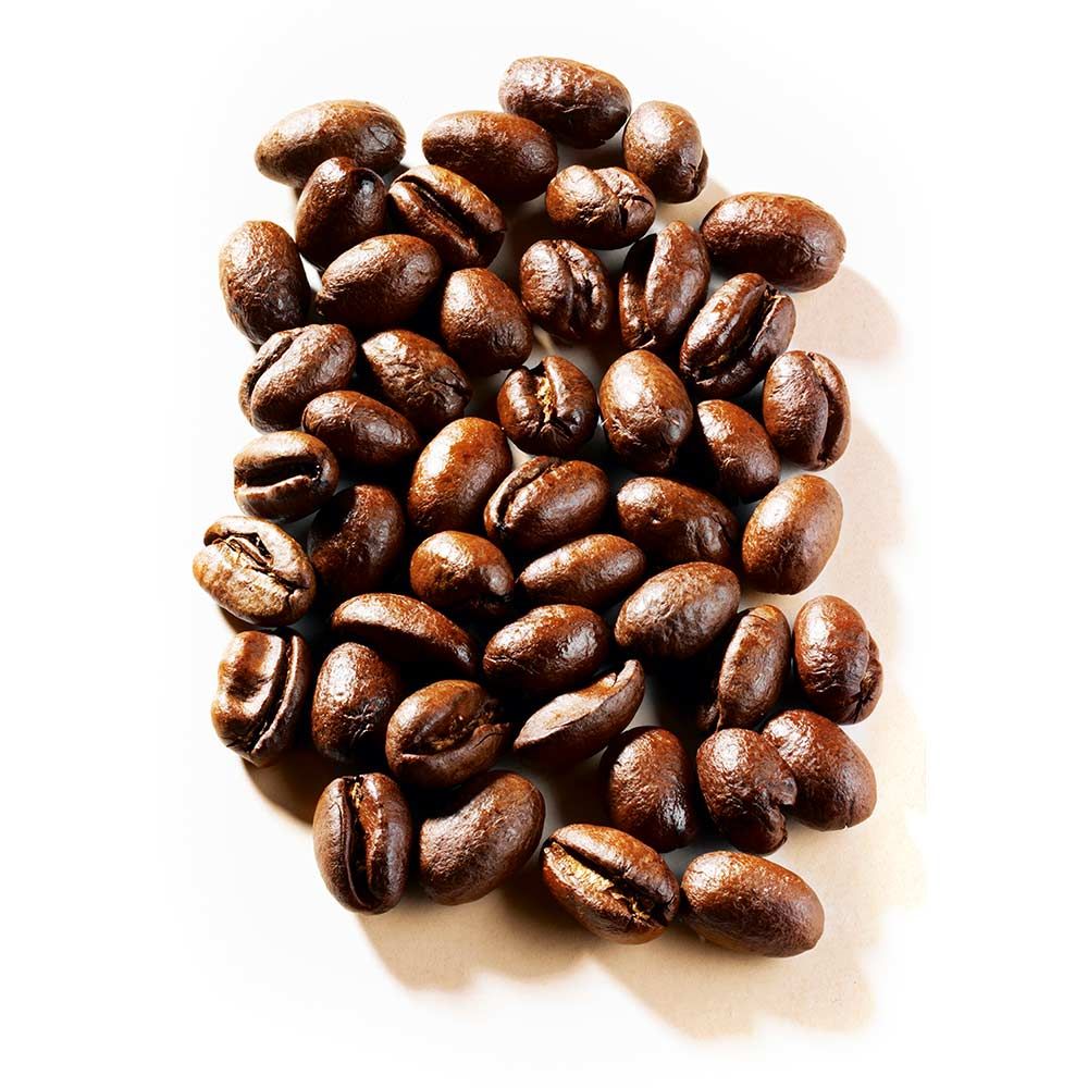 Haufen gerösteter Kaffeebohnen auf weißem Hintergrund. Einzelne Bohnen sind sichtbar.