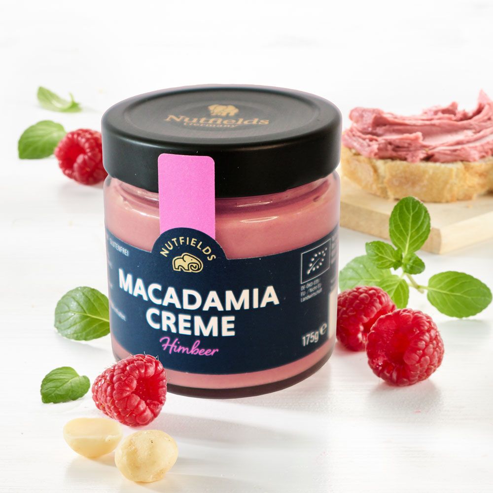 Glas Macadamia Creme mit Himbeer-Etikett. Himbeeren und Blätter daneben. Bio-Siegel.