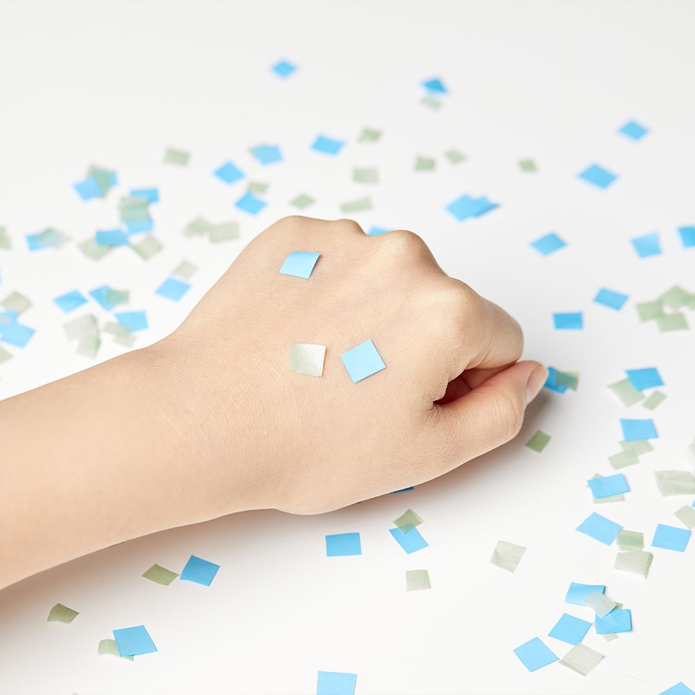 Hand mit blauen und grünen Konfetti-Quadraten.