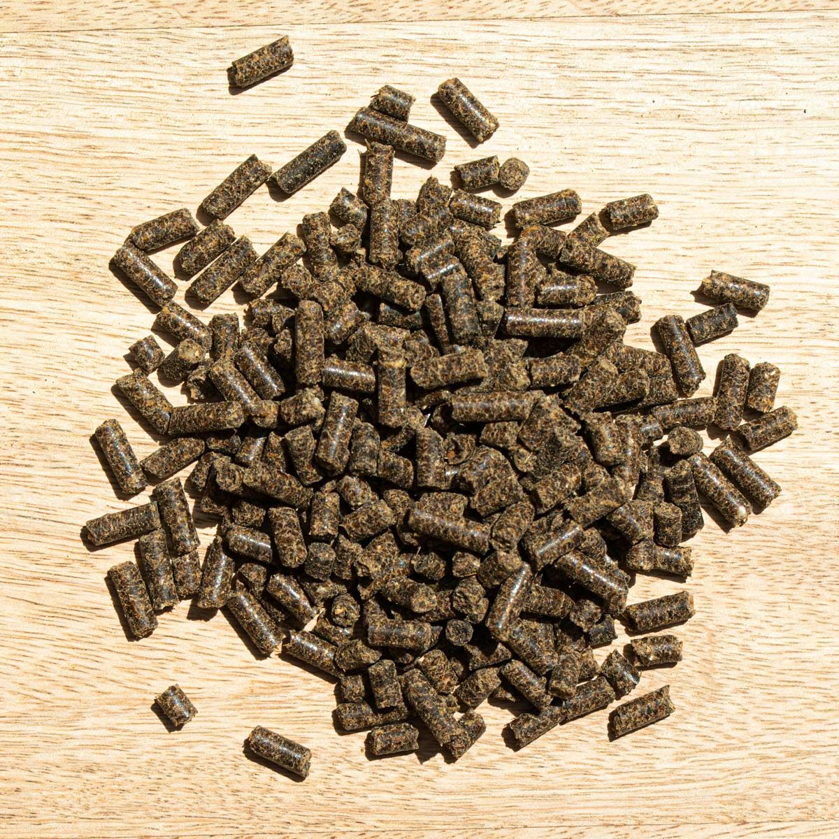 Haufen brauner Pellets auf Holzoberfläche. Oben-Ansicht. Pellets sind zylindrisch und unregelmäßig geformt.