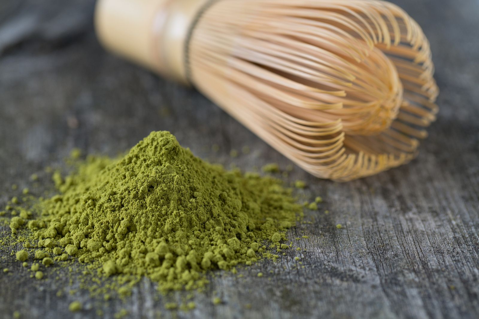 Haufen grünes Pulver und Bambus-Matcha-Besen auf Holzoberfläche.