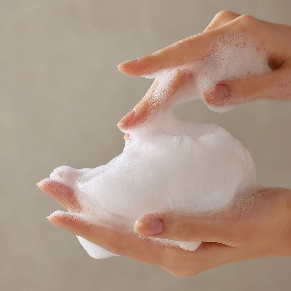 Hände mit weißem Schaum. Der Schaum wird zwischen den Fingern gehalten.