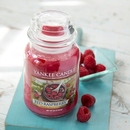 Rote Duftkerze im Glas mit Deckel. Etikett mit Aufschrift "Red Raspberry". Daneben Himbeeren in Schale.