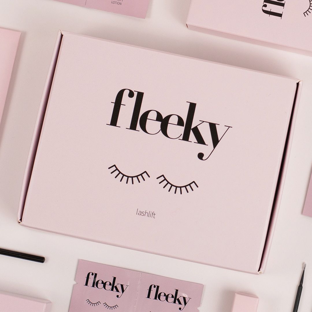 Rosa Karton mit Aufdruck: fleeky, Lashlift. Gezeichnete Wimpern. Zubehörteile liegen um die Box herum.