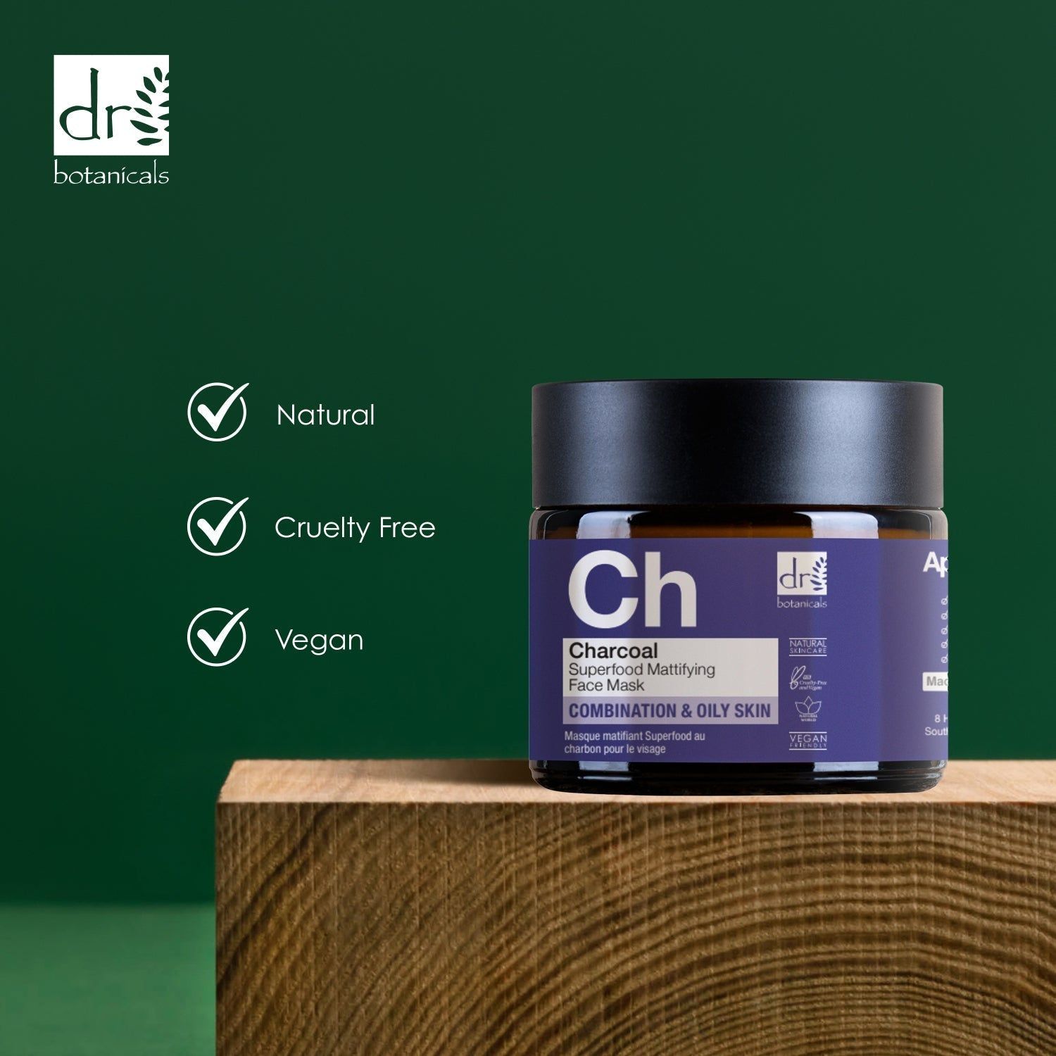 Tiegel auf Holzblock. Dunkelbraunes Glas mit schwarzem Deckel. Violettes Etikett. 3 grüne Häkchen: Natural, Cruelty Free, Vegan.