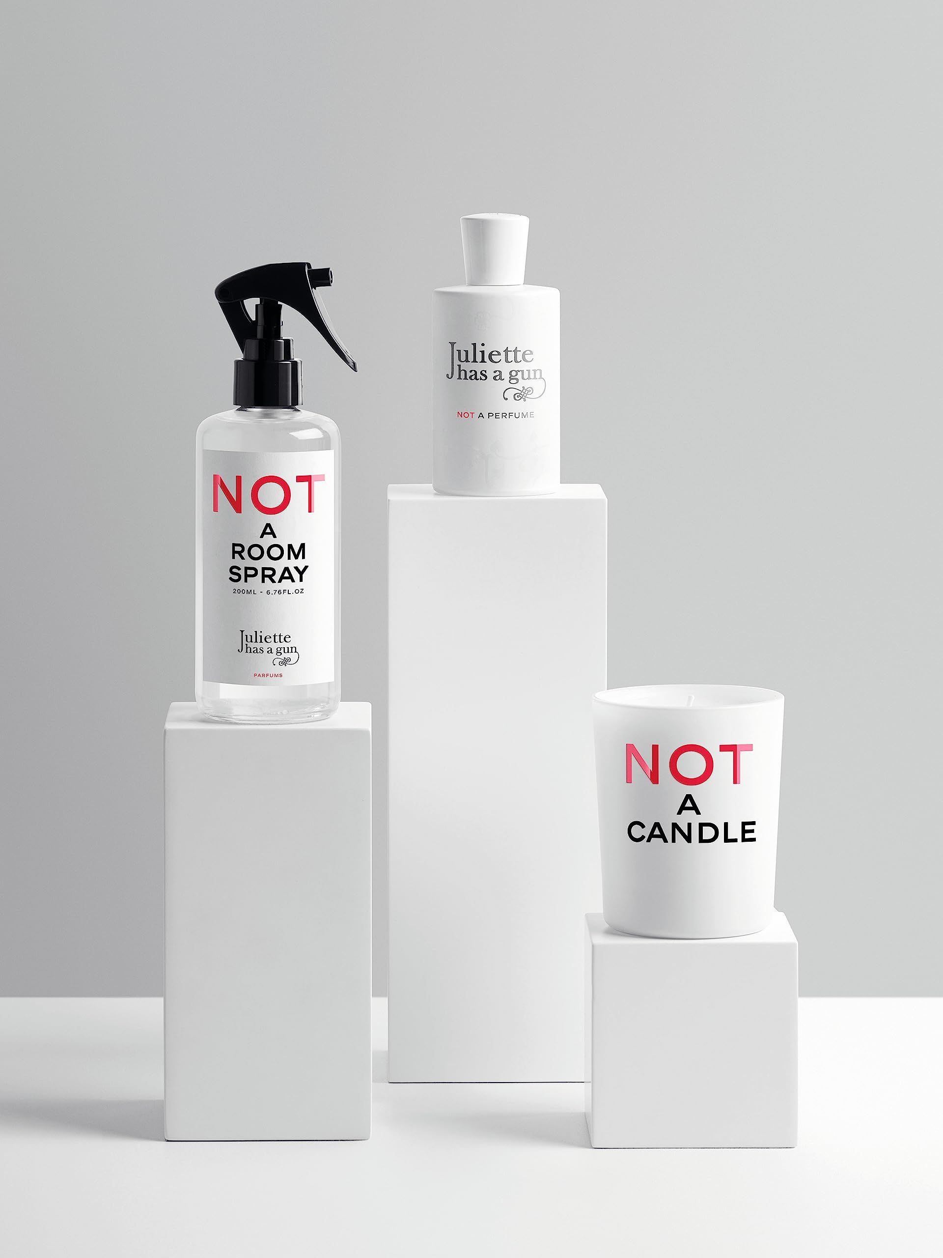 Drei Produkte auf weißen Podesten: Raumduft, Parfümflasche und Kerze. Aufschrift 'NOT A CANDLE' und Markenname.