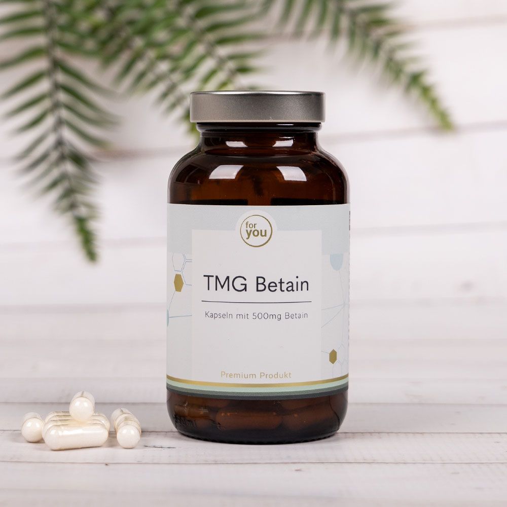 Braune Glasflasche mit silbernem Deckel und Etikett "for you TMG Betain". Daneben Kapseln.