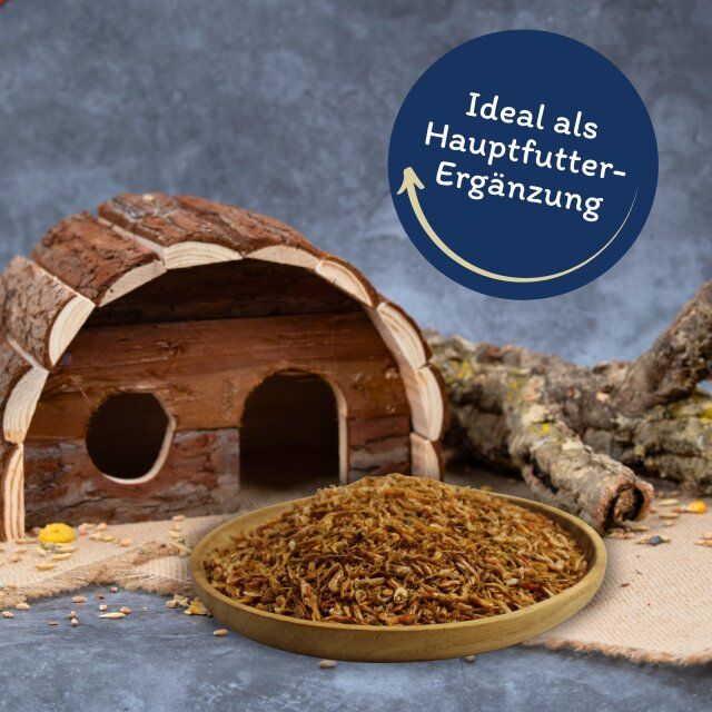 Getrocknete Shrimps in einer Holzschale. Aufschrift: Ideal als Hauptfutter-Ergänzung. Im Hintergrund: Holzhaus.
