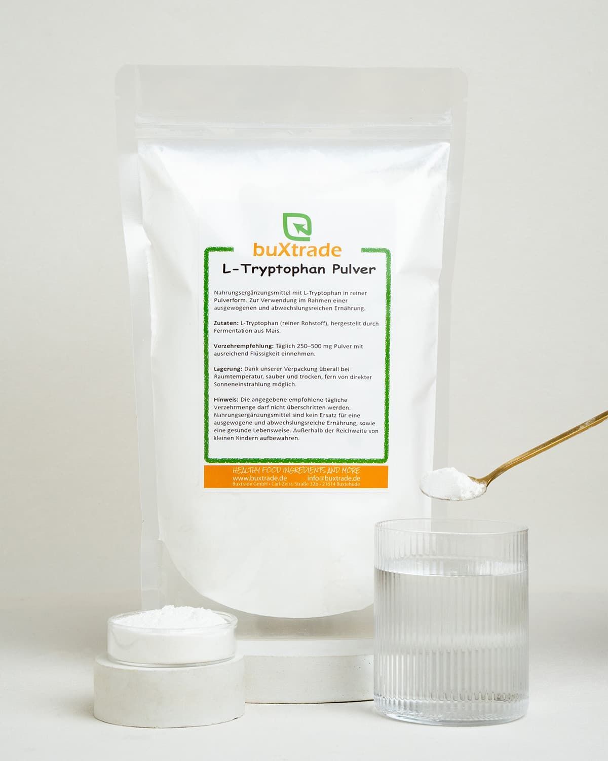 Ein Beutel L-Tryptophan Pulver von buxtrade, daneben ein Glas Wasser, ein Löffel mit Pulver und eine kleine Schale mit Pulver.