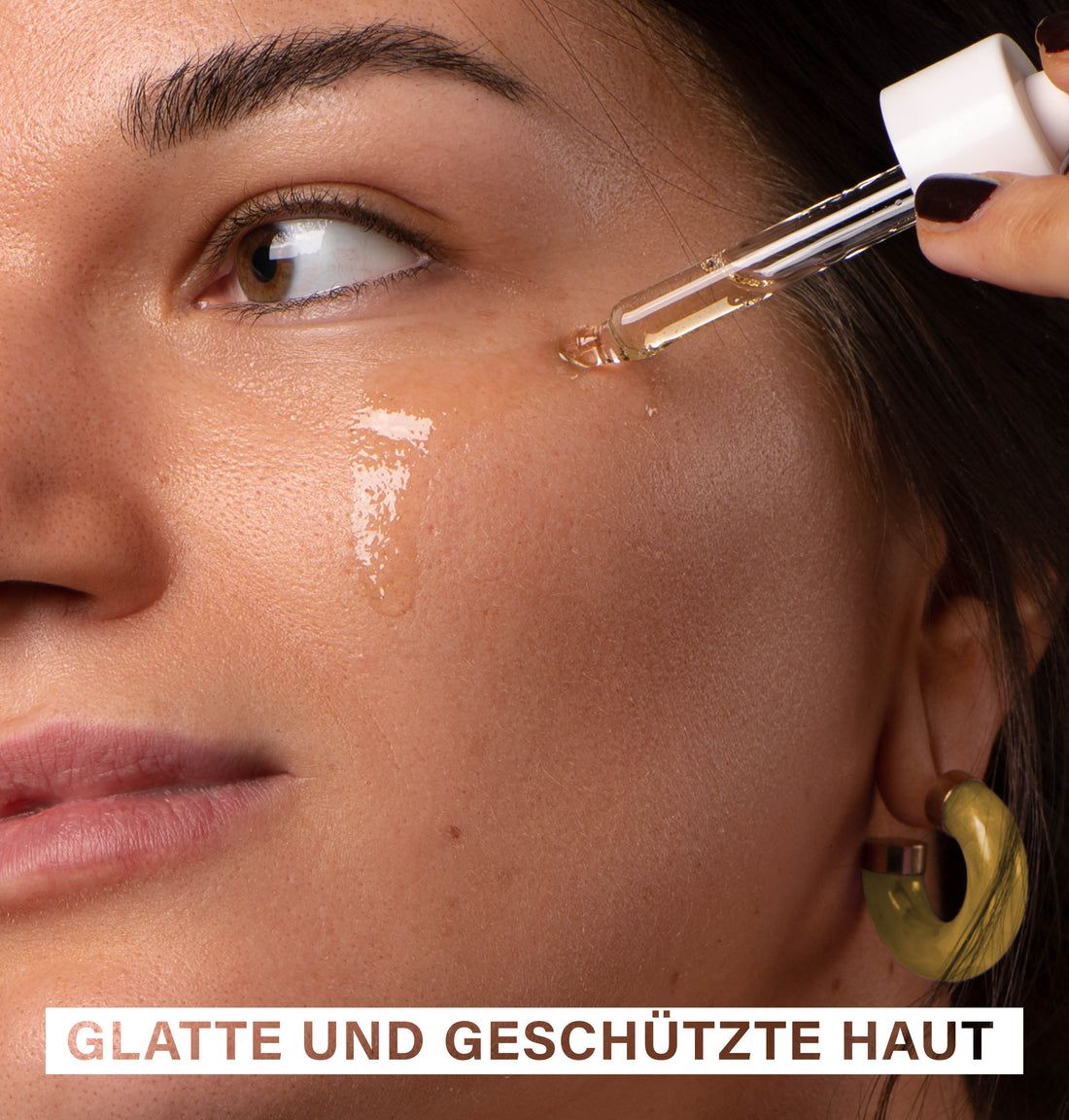 Nahaufnahme einer Frau, die Marula Oil mit einer Pipette auf ihre Wange aufträgt. Text: Glatte und geschützte Haut.