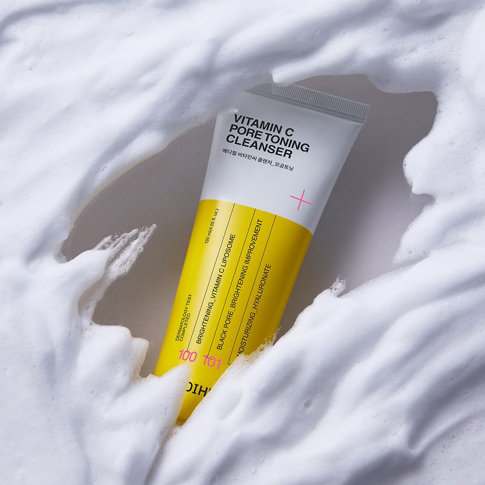 Eine weiße Tube mit gelbem Etikett, die Vitamin C Pore Toning Cleanser enthält. Umgeben von Schaum.
