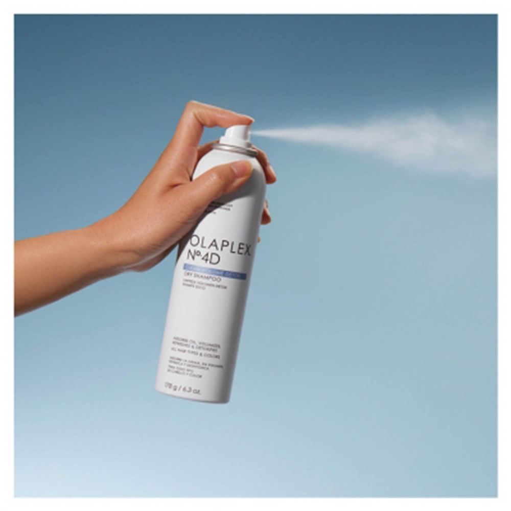 Hand sprüht Olaplex Nº4D Trockenshampoo-Spray. Sprühnebel ist sichtbar.