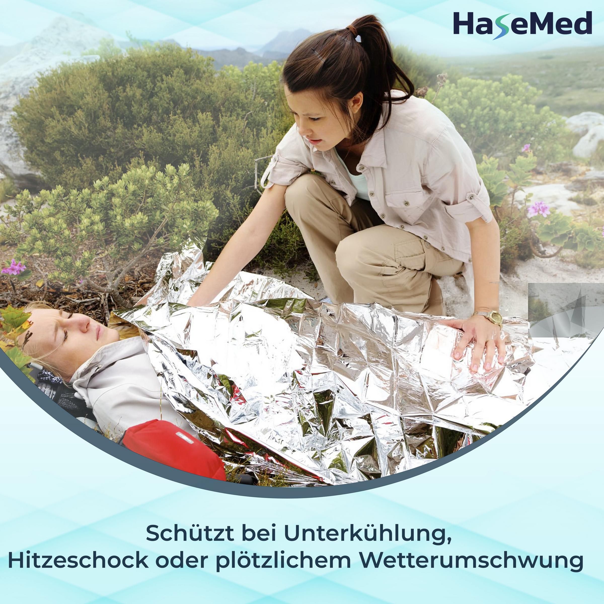 Person wird mit silberner Rettungsdecke bedeckt. Frau kniet daneben. Text: Schützt bei Unterkühlung, Hitzeschock oder plötzlichem Wetterumschwung.