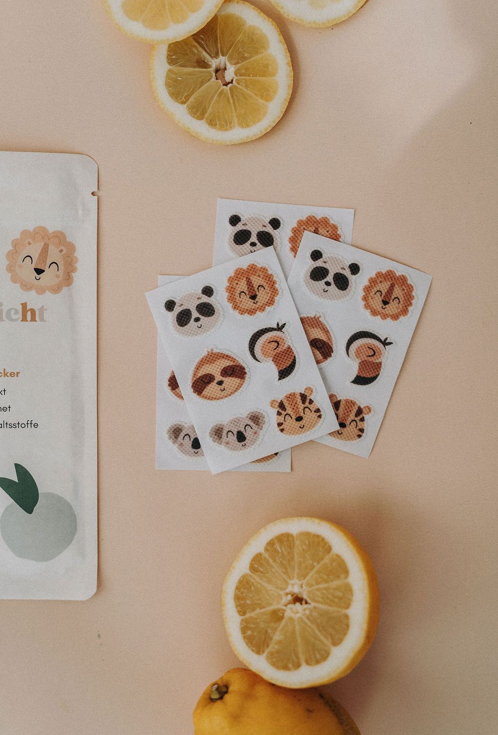 Mehrere Stickerbögen mit Tiergesichtern, daneben eine Packung und Zitronenscheiben. Aufkleber mit Panda, Löwe, Faultier, Koala, Tiger und Tukans.